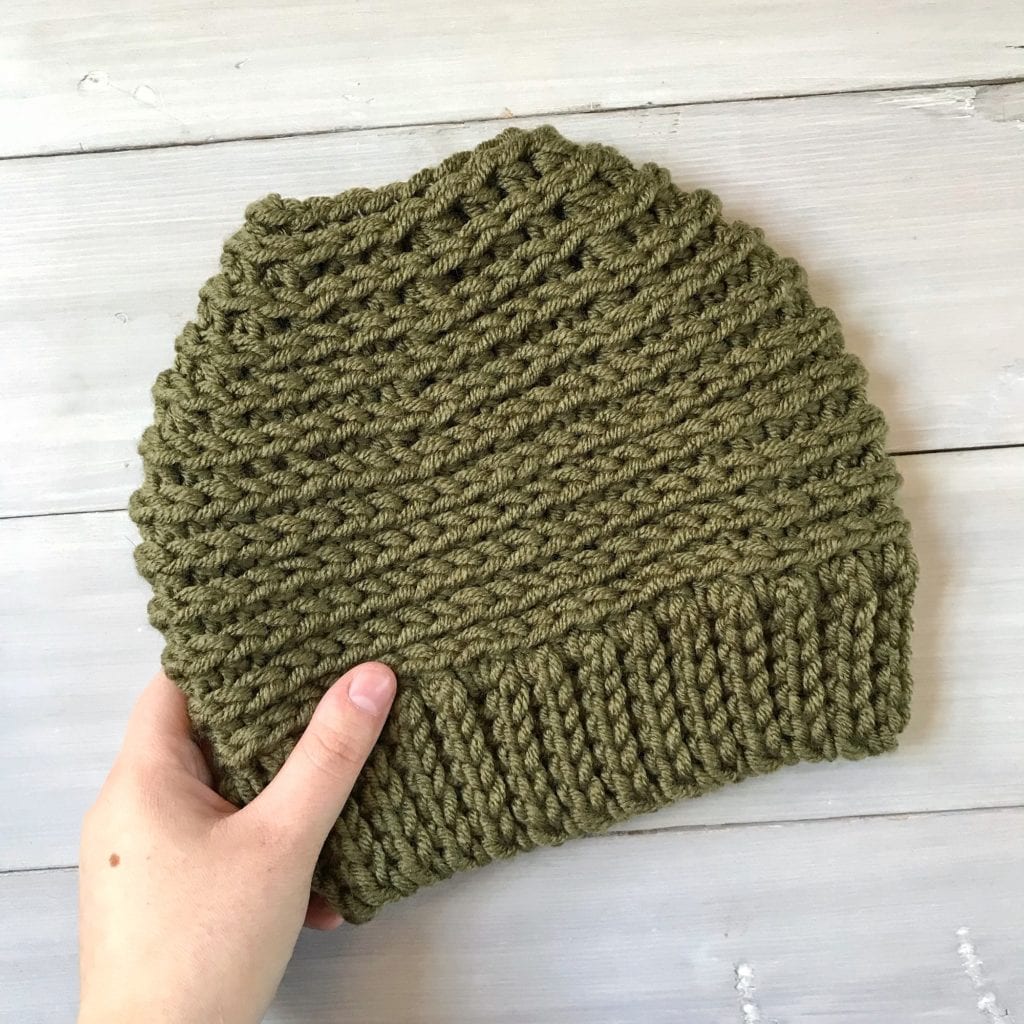 Hand holding an army green crochet messy bun hat